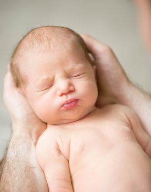 Portrait of a newborn hold in male palms, eyes closed. Family, healthy birth concept photo.